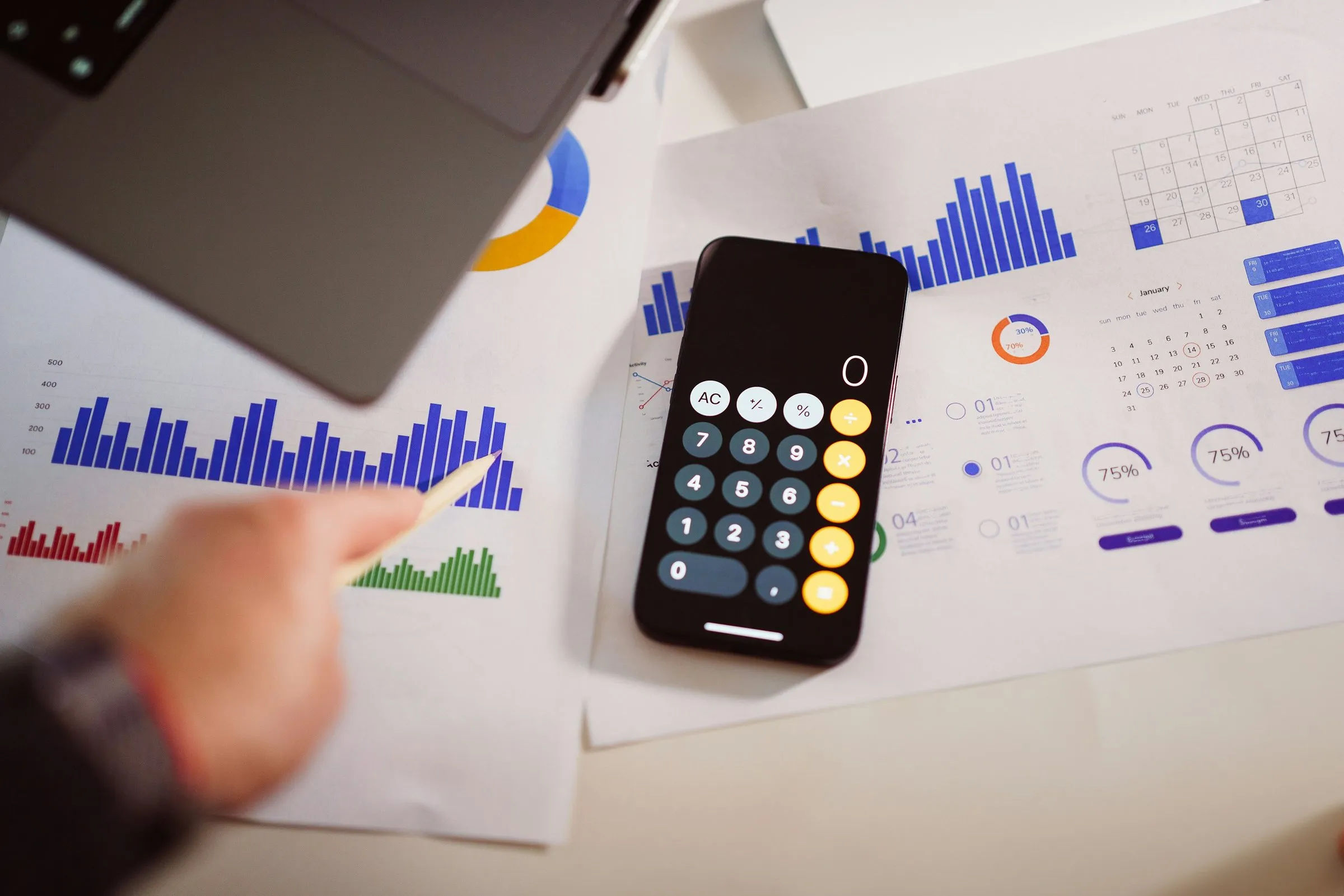 Printed bar charts and a calculator on a desk, with a hand resting beside them.