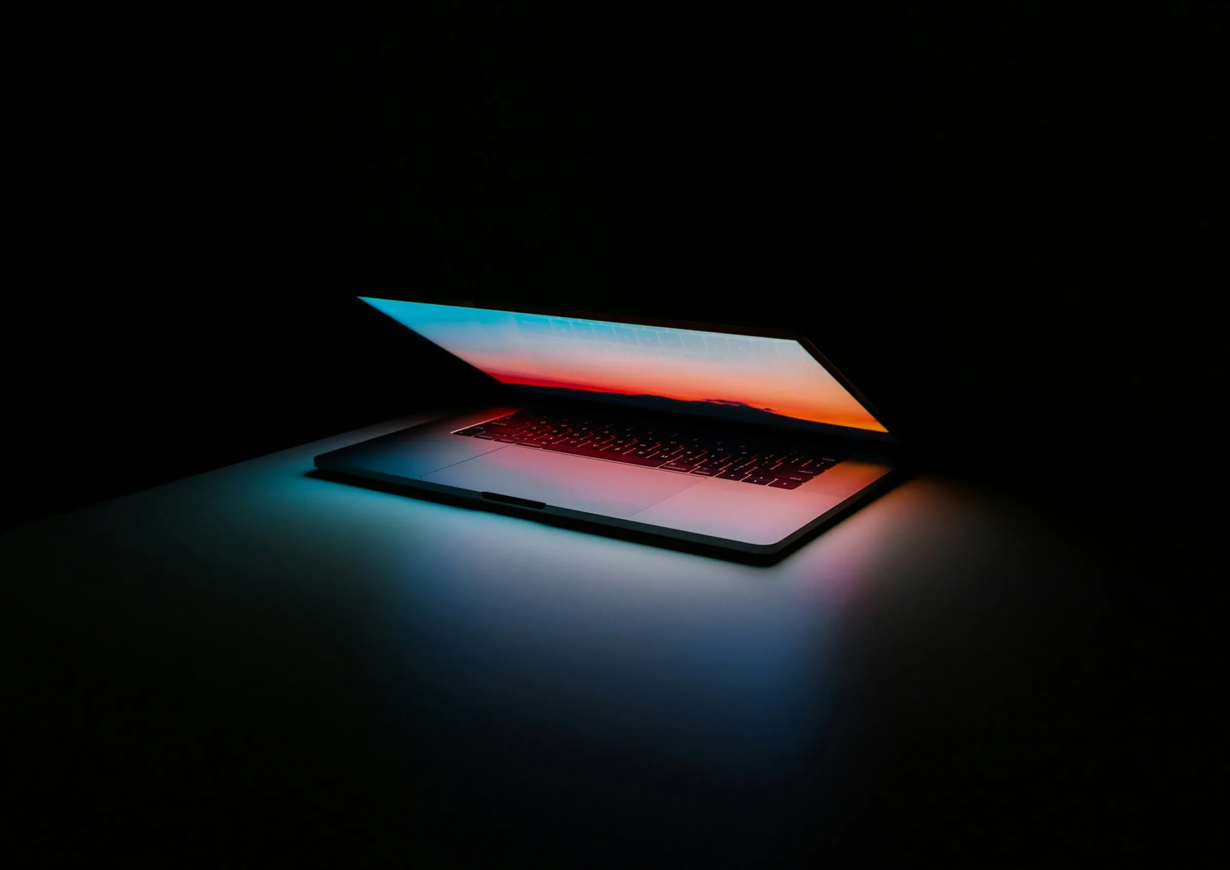 An open laptop lit from within against a black background, the screen too bright to read.